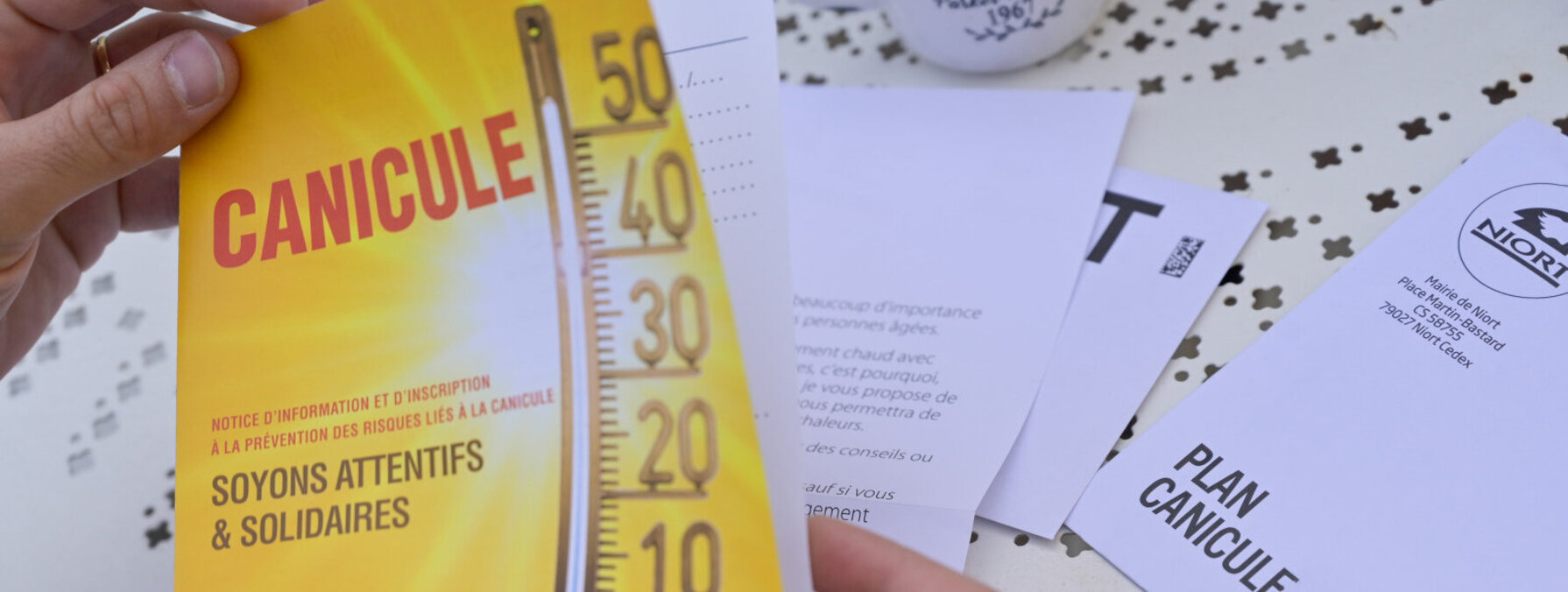 Brochure Plan Canicule de la Ville de Niort tenue en main, avec thermomètre et slogan « Soyons attentifs & solidaires »